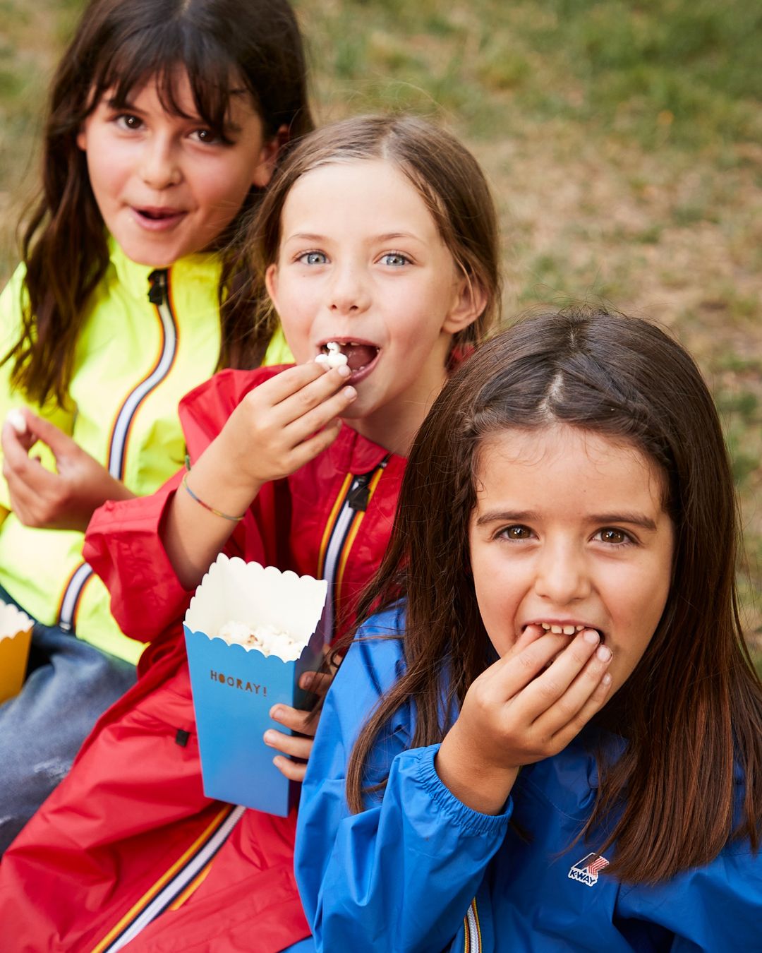 Kids eating pop corn outside wearing colorful K-Way Claude Jackets