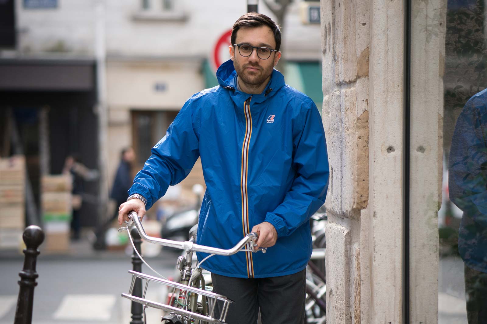 Men wearing a Claude Amiable Recycled and Sustainable Jacket in Blue Royal while walking next to his bike in a city street.